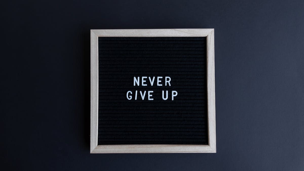 Inspirational letter board with 'Never Give Up' phrase on gray background.